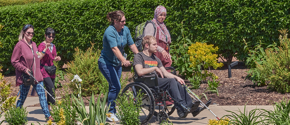 Guests walk through The Gerard T. Donnelly Grand Garden with a wheelchair and a walking stick