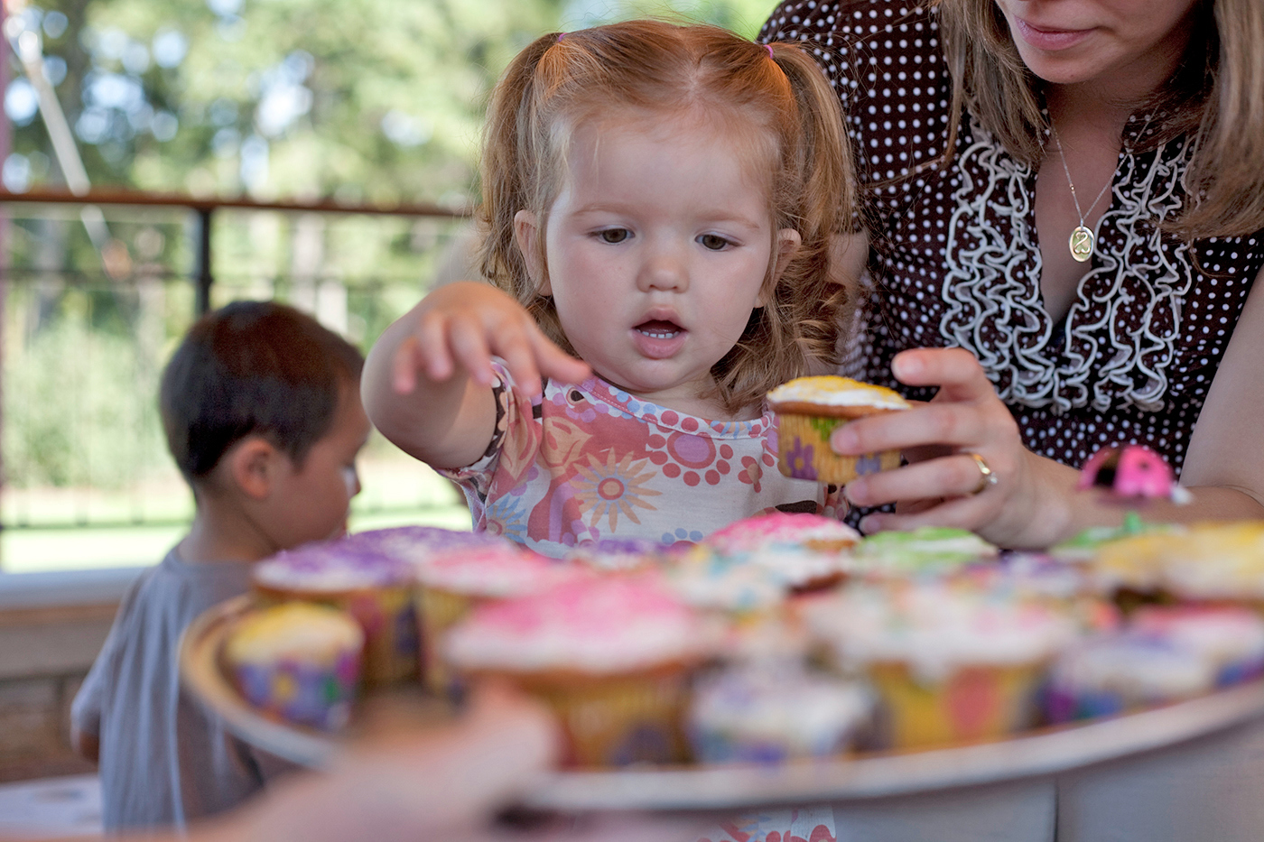 Child reaches for a cupcake at her birthday party