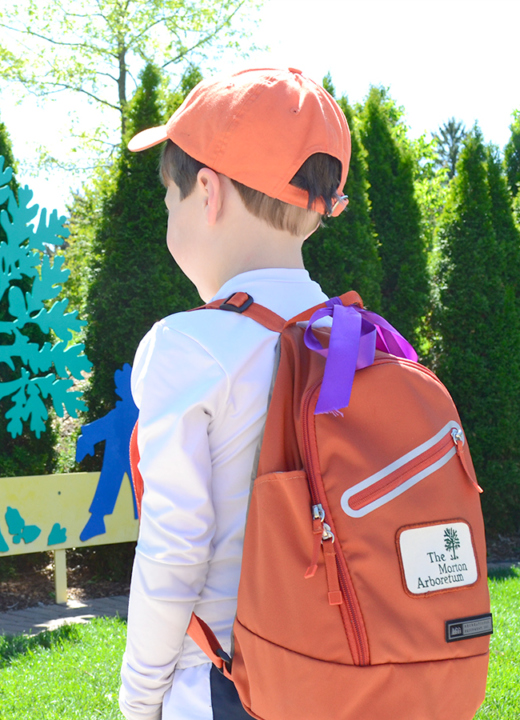 A child wearing an orange ball cap and orange backpack walks into the Children's Garden.
