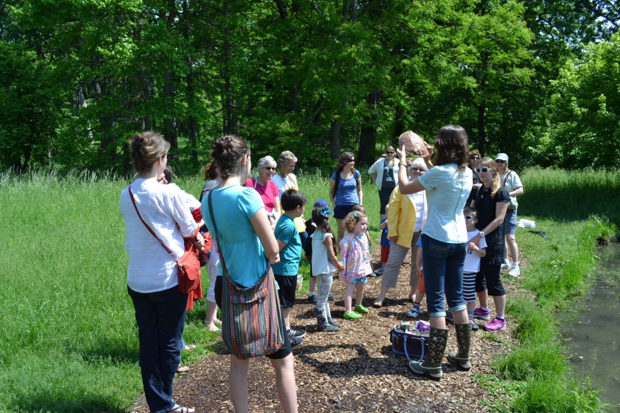 Group of students with parents gathered around teacher holding a turtle shell by a lake